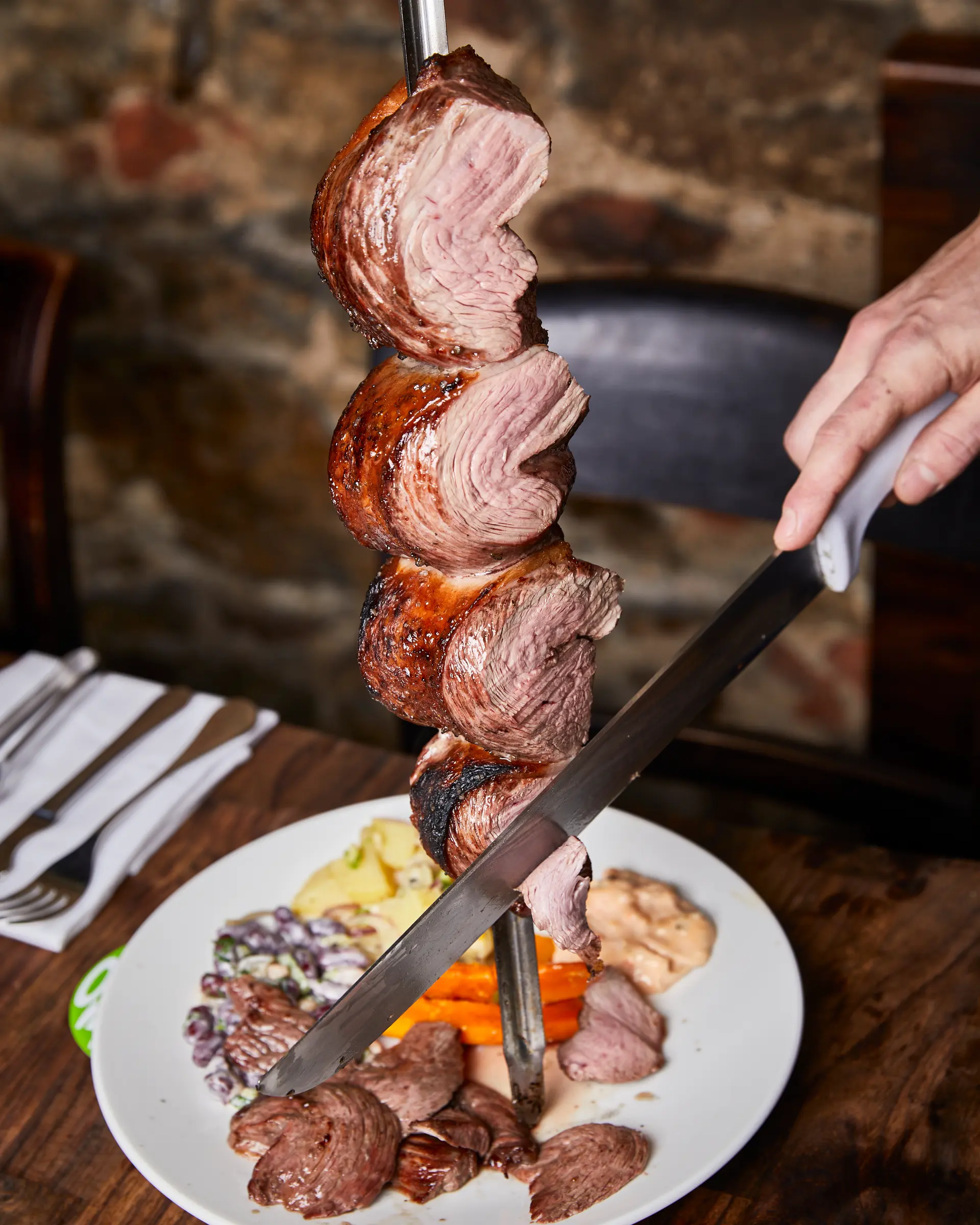 Passador slicing grilled beef directly onto the plate at Brasileiro restaurant.
